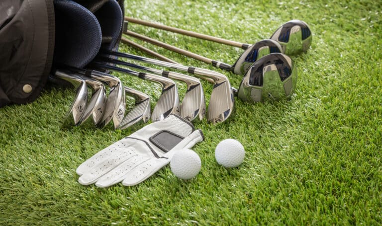 Golf Clubs for Beginners – Best Guide to Get Started 1 A set of golf clubs, a white golf glove, and two golf balls on a green grass surface.