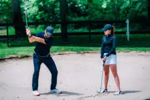 professional golf lessons in Phuket: A golf instructor demonstrating a bunker shot to a female golfer.