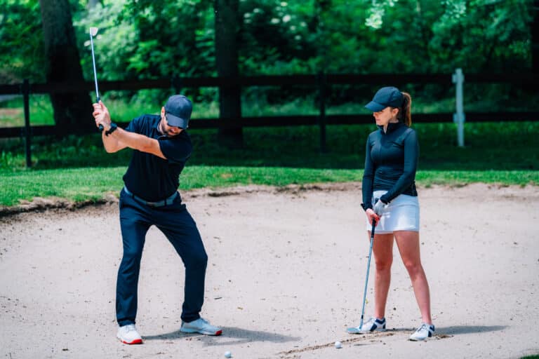 professional golf lessons in Phuket: A golf instructor demonstrating a bunker shot to a female golfer.