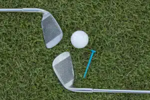 iron play: Golf ball, irons, and tee on the grass.