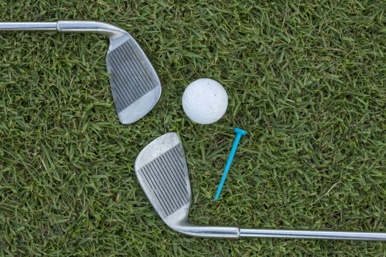 iron play: Golf ball, irons, and tee on the grass.