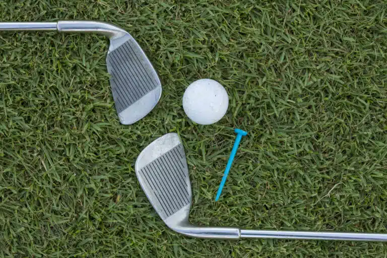 iron play: Golf ball, irons, and tee on the grass.