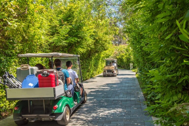 Things to do on a golf holiday in Phuket: Golf carts transporting people and luggage on a scenic path.