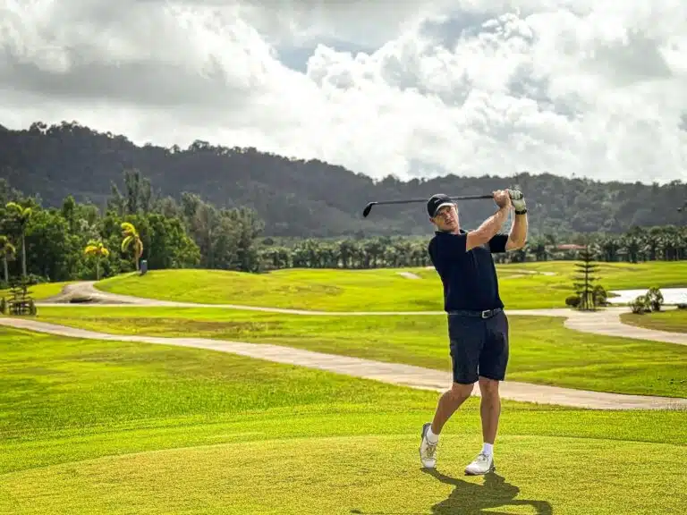 Personal golf trainer in Phuket: Golfer finishing a swing on a scenic golf course.