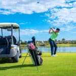 golf experience in Phuket: Golfer taking a swing by a lake with a golf cart nearby.