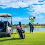golf experience in Phuket: Golfer taking a swing by a lake with a golf cart nearby.