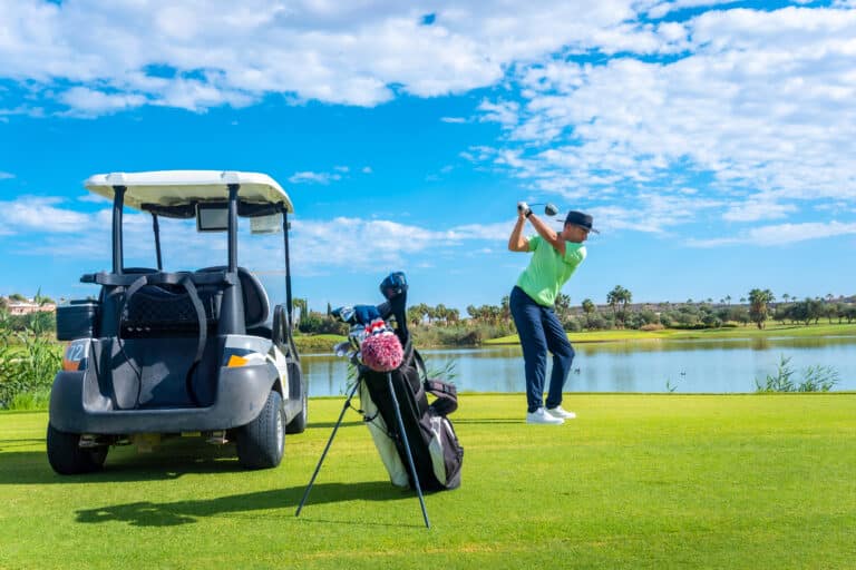 Ultimate Golf Experience in Phuket – Play in Luxury 3 golf experience in Phuket: Golfer taking a swing by a lake with a golf cart nearby.